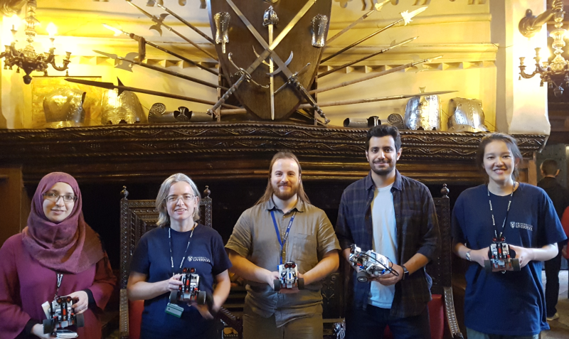 A picture of Farah, Louise, Matt, Mohammad, and Xia (left to right) on the Great Hall at Speke Hall, each holding a Lego Rover